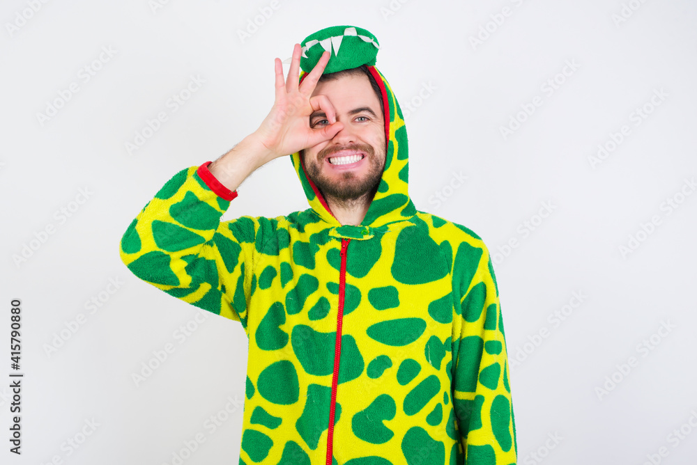 Fototapeta premium young caucasian man wearing a pajama standing against white wall doing ok gesture with hand smiling, eye looking through fingers with happy face.