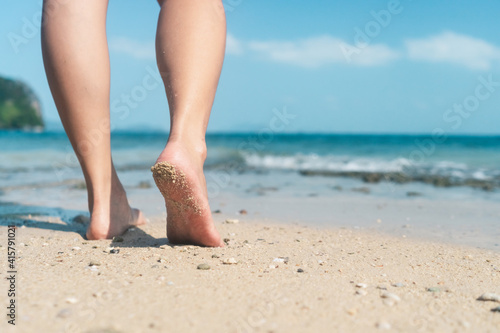Woman feet walk slow life and relax on sand tropical beach with blue sky background.