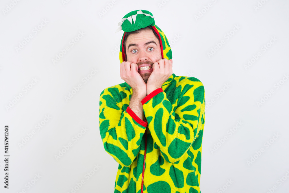 Fototapeta premium Fearful young caucasian man wearing a pajama standing against white background keeps hands near mouth, feels frightened and scared, has a phobia, Shock and frighted concept.