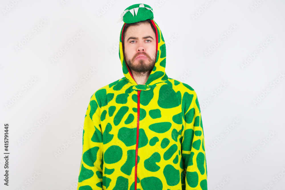 Fototapeta premium Displeased upset young caucasian man wearing a pajama standing against white wall frowns face as going to cry, being discontent and unhappy as can't achieve goals, Disappointed model has troubles