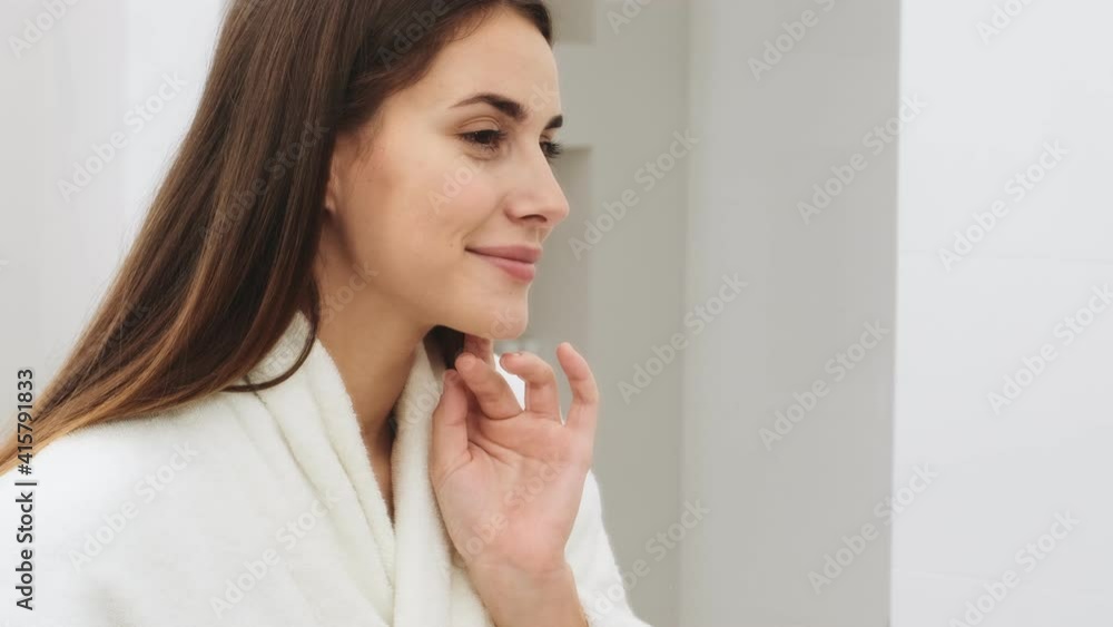 A smiling young woman is looking to the mirror standing in the apartments A smiling young woman is looking to the mirror standing in the apartments