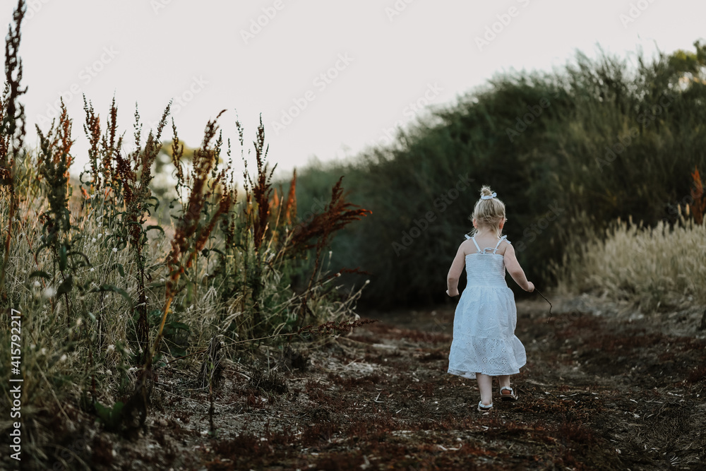 Beautiful little girl in white dress walking along dry creek bed at sunset Beautiful little girl in white dress walking along dry creek bed at sunset