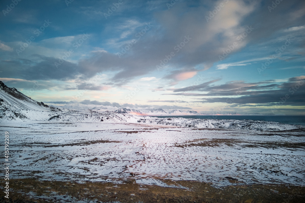 Snow-covered arctic landscape. Winter in Iceland nature - vast plains snow-capped distant mountains and rippled water surface.