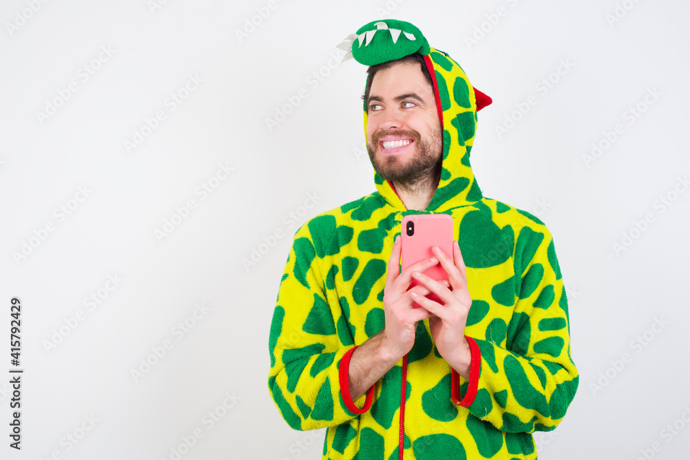Fototapeta premium young caucasian man wearing a pajama standing against white background hold telephone hands read good youth news look empty space advert