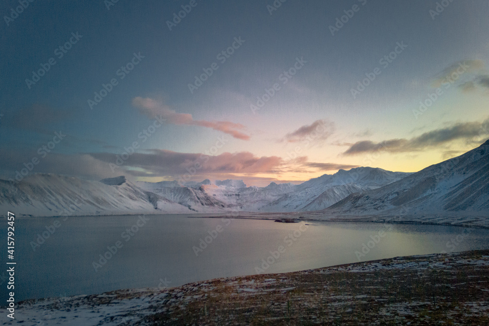 View on vast water lagoon bordered by mountains. Snow-covered arctic landscape after sunset. Twilight time in Iceland.