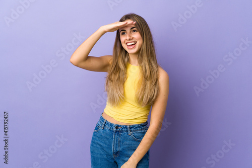 Young woman over isolated purple background looking far away with hand to look something