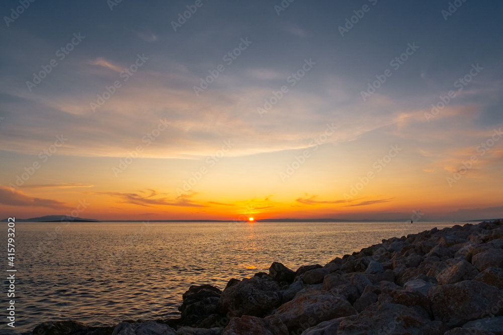 Multi-coloured twilight sky above vast water surface. Sun rising behind mainland and Adriatic sea. Romantic scene.
