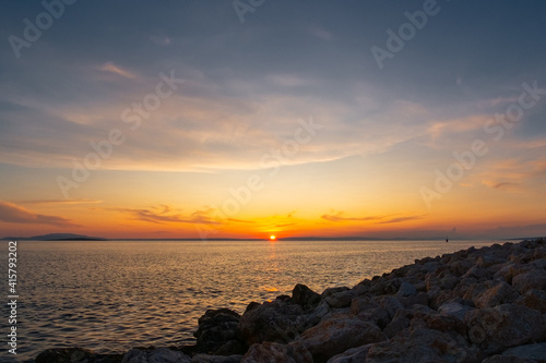 Multi-coloured twilight sky above vast water surface. Sun rising behind mainland and Adriatic sea. Romantic scene.