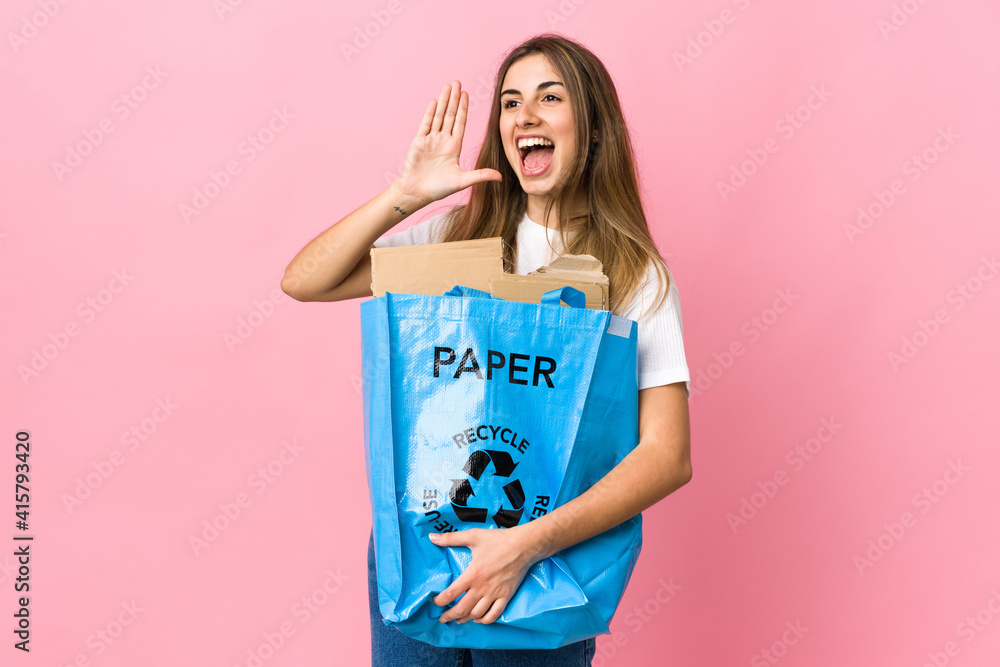 holding a recycling bag full of paper to recycle over isolated pink shouting with mouth wide open holding a recycling bag full of paper to recycle over isolated pink shouting with mouth wide open
