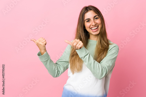 Young woman over isolated pink background pointing to the side to present a product © luismolinero