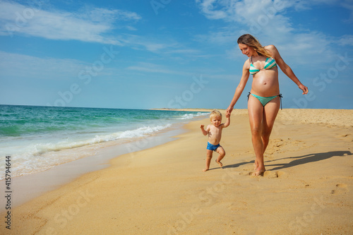 Little blond toddler boy walk with mother play near sea waves water holding hands