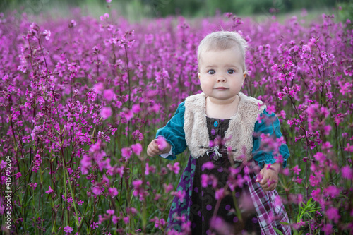 blond baby in a colored dress standing in a field with purple flowers