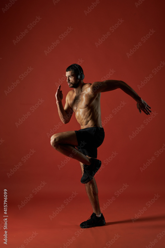 Focused athlete man in headphones doing fitness exercises isolated on red background