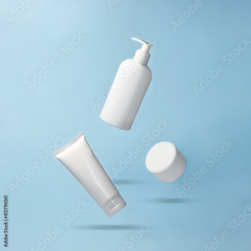 White jar and bottles for cosmetics products flying on blue background. Levitation. Body care creative concept. Mock up