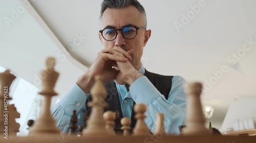 A close-up cropped view of a nervous man is playing chess sitting inside