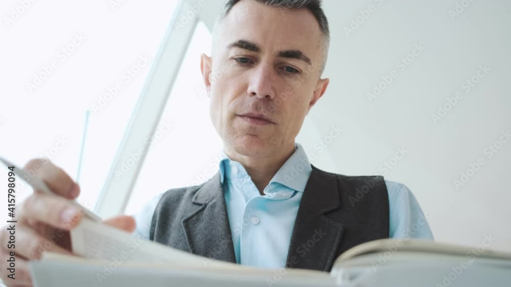 A serious adult man is working with paper documents sitting inside the public space A serious adult man is working with paper documents sitting inside the public space