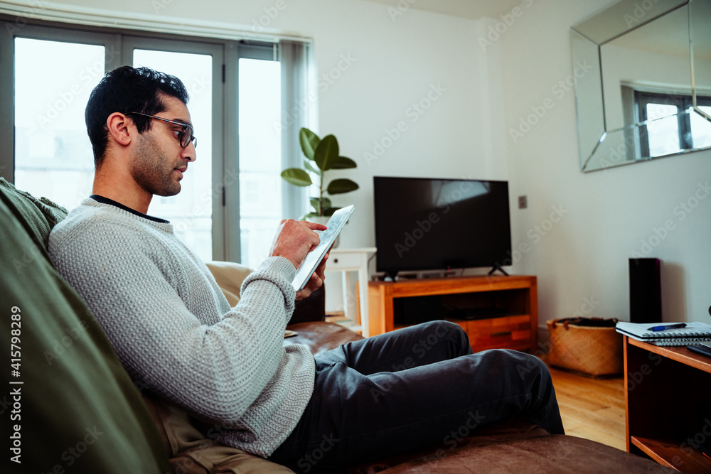 Mixed race business man sitting on couch scrolling on digital tablet working from home Mixed race business man sitting on couch scrolling on digital tablet working from home