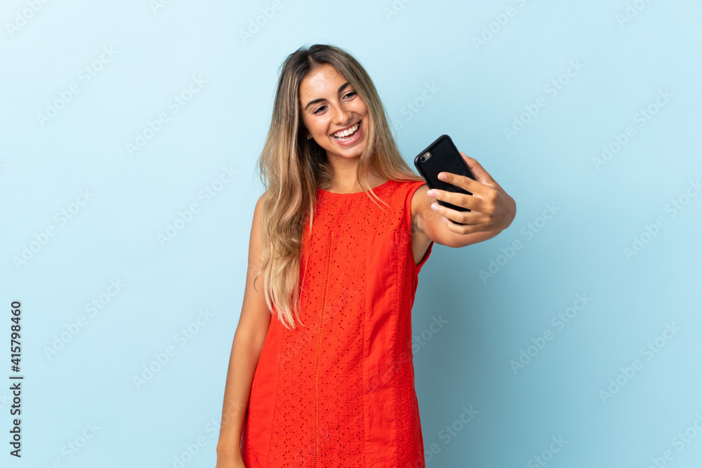 Fototapeta premium Young hispanic woman over isolated blue background making a selfie