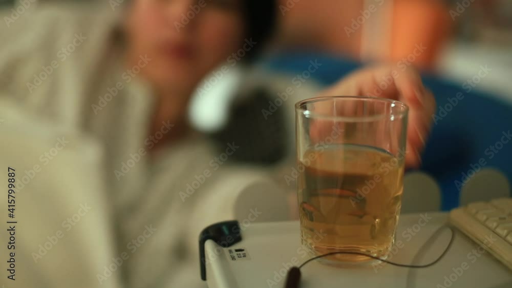 Increased water balance patient places a glass of drink on a stand in a dark room. Relaxation lying on the bed. Restoration of strength, regeneration of energy.