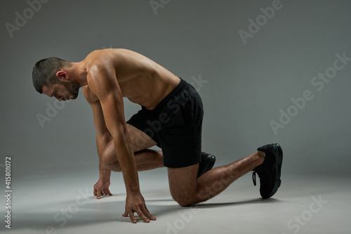 Adorable focused athlete man in shorts and sneakers taking a breather in room indoors