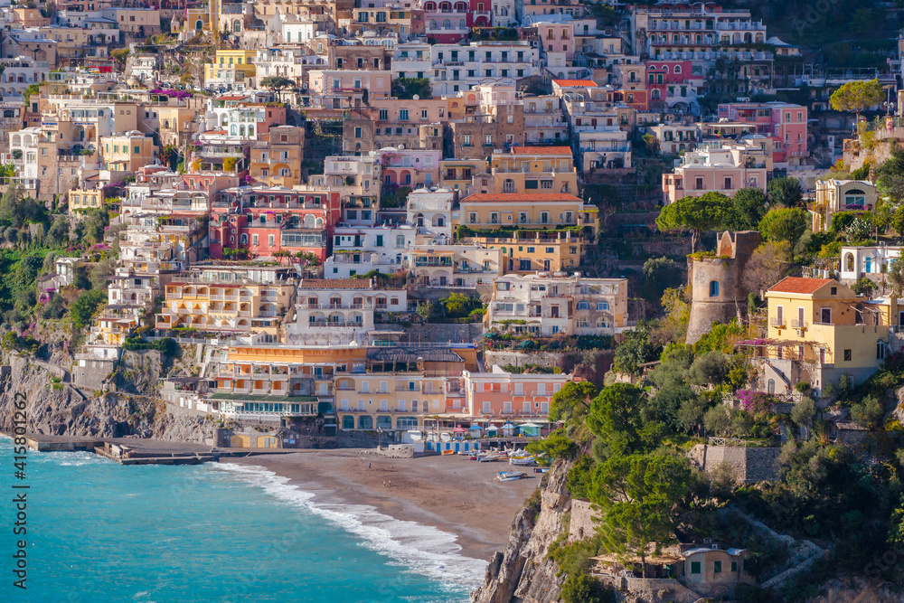 Green trees, sandy beach and colorful Amalfi houses on hills leading down to coast, Campania, Italy.