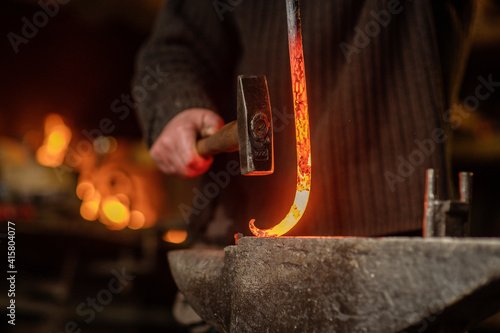 The blacksmith hits the red-hot workpiece in the forge with a hammer and glowing sparks fly in all directions photo