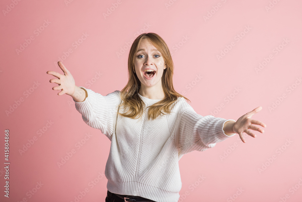 Beautiful young girl on a pink background in the studio stretches out her arms for a hug Beautiful young girl on a pink background in the studio stretches out her arms for a hug
