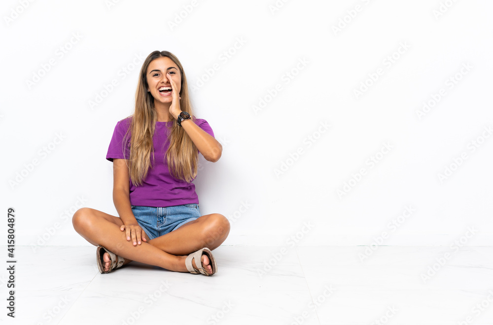 Young hispanic woman sitting on the floor shouting with mouth wide open