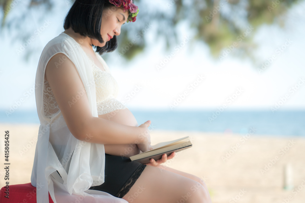 Obraz premium Asian Pregnant woman reading a book with copy space. (Vintage tone) at beach .Young pregnant woman .