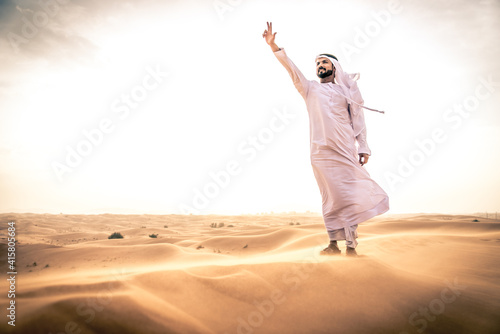 Arabic man with traditional emirates clothes walking in the desert photo