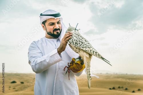 Arabic man with traditional emirates clothes walking in the desert with his falcon bird photo