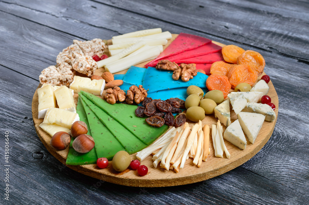 Different kinds of cheeses, dried apricots, whole-grain breads, nuts, olives, capers on a wooden board. Cheese board, snacks. Different kinds of cheeses, dried apricots, whole-grain breads, nuts, olives, capers on a wooden board. Cheese board, snacks.