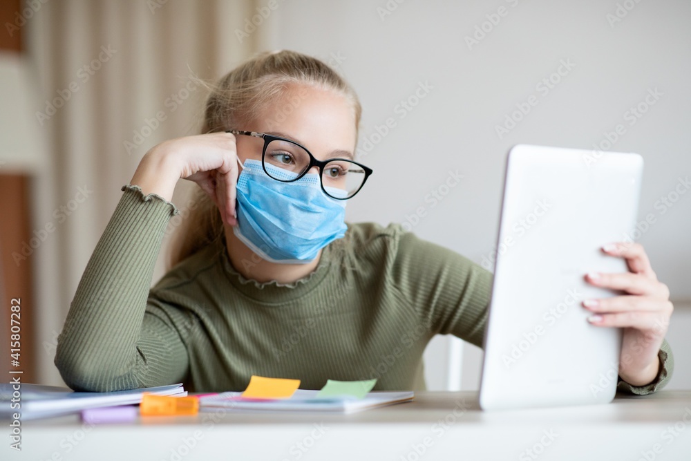 Bored teen girl in face mask using digital tablet Bored teen girl in face mask using digital tablet