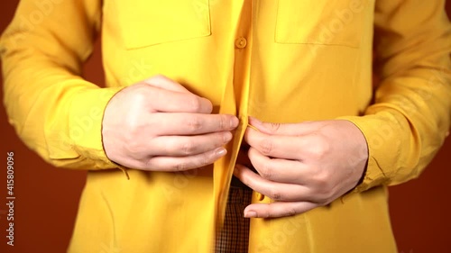 Front view on body part of young female in yellow blouse. Close up of unrecognizable woman unbutton her blouse on orange background.
