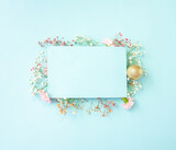 Bright Easter spring creative layout. Flowers of gypsophila and carnations of white and pastel pink colors with gold egg on a light blue background with copy space. Flat lay. Top view.