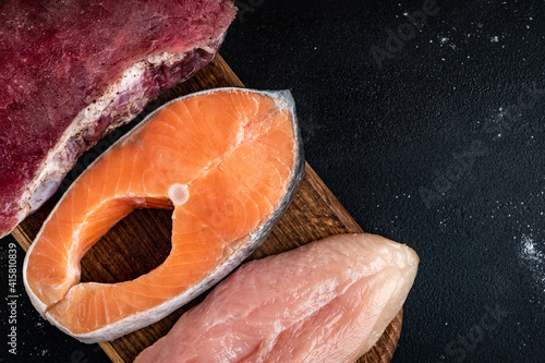 Fresh raw meat, salmon and chicken fillet on wooden cutting board on black background. Natural food high in protein. Top view. photo