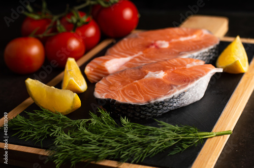 Blurred image of raw salmon steak with lemon and herbs, tomatoes.