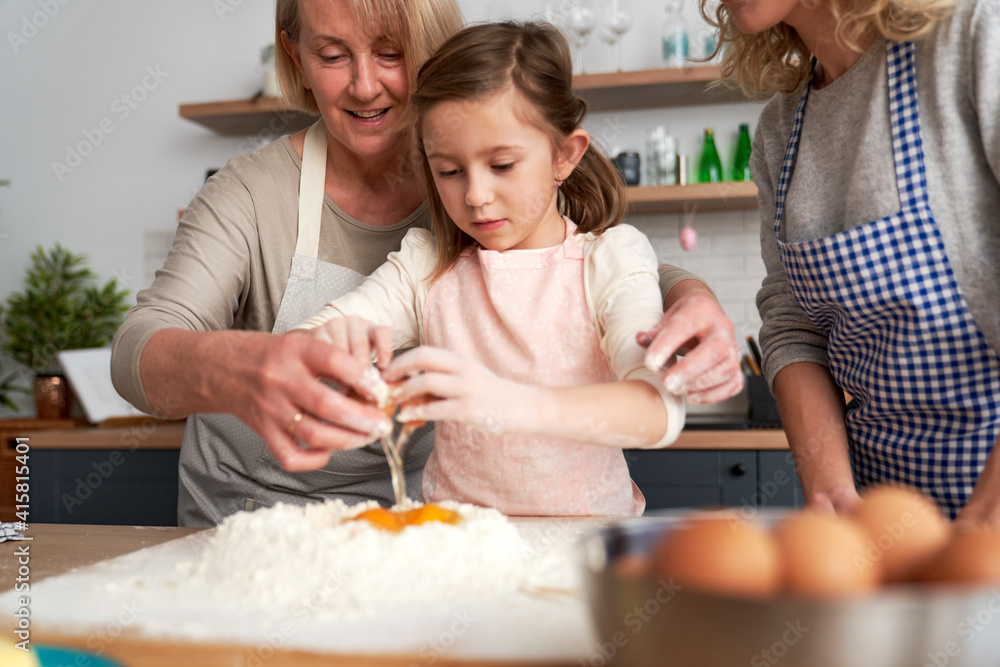Little girl with grandmother breaking an egg into the flour Little girl with grandmother breaking an egg into the flour