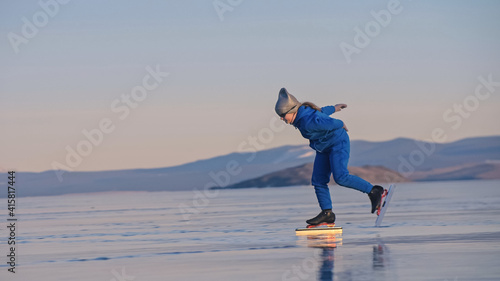 The girl train on ice speed skating. The child skates in the winter in blue sportswear suit, sport glasses. Children speed skating sport. Outdoor slow motion. Snow capped mountains, beautiful ice.