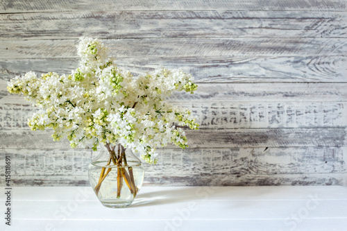 White lilac bouquet in glass vase on wooden table. Spring branches of blooming lilac festive bouquet of flowers with copy space.