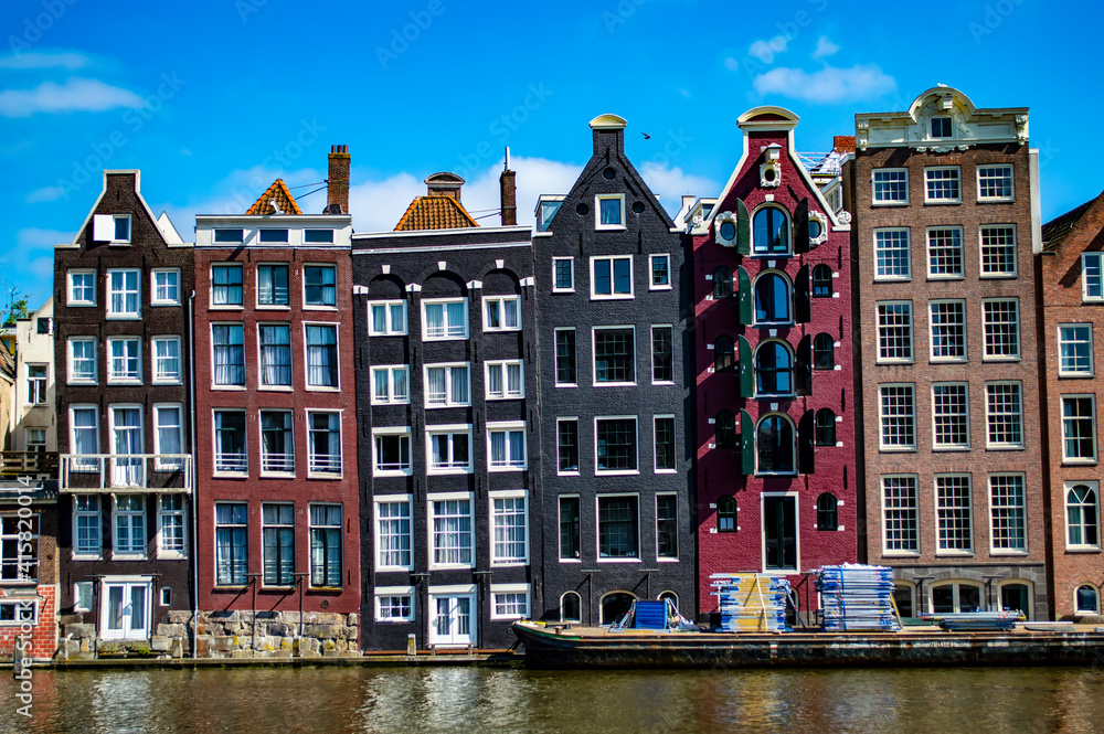 Amsterdam, Netherlands - June 27, 2019: Cargo boat docked by the dancing houses at Damrak in Amsterdam, the capital of the Netherlands