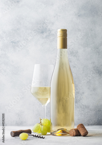 Glass and bottle of summer white wine with grapes, corks and corkscrew on light background.
