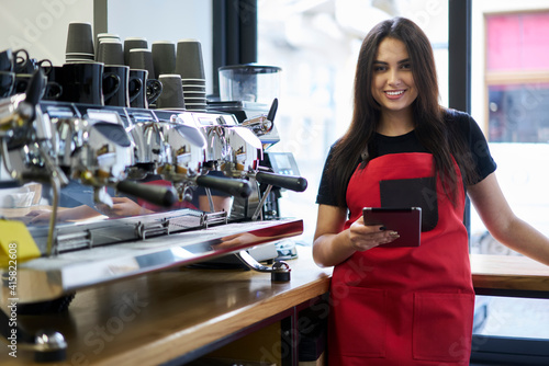 Half length portrait of cheerful caucasian woman barista using digital tablet app for checking orders online, smiling experiencer girl waitress using gadget for organizing job process in coffee house photo
