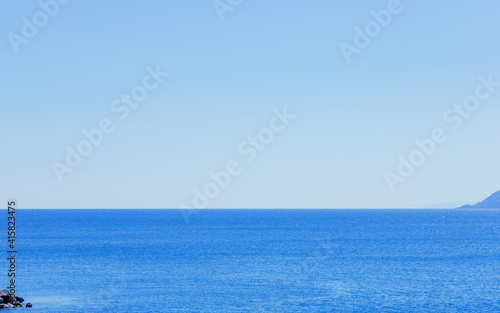 Seascape with light blue skies, blue sea, cliff islands and a distant horizon.