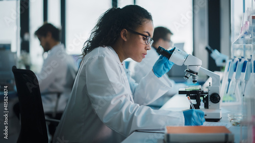 Medical Science Laboratory: Beautiful Black Scientist Looking Under Microscope Does Analysis of Test Sample. Diverse Team of Young Specialists, Using Advanced Technology Equipment. photo