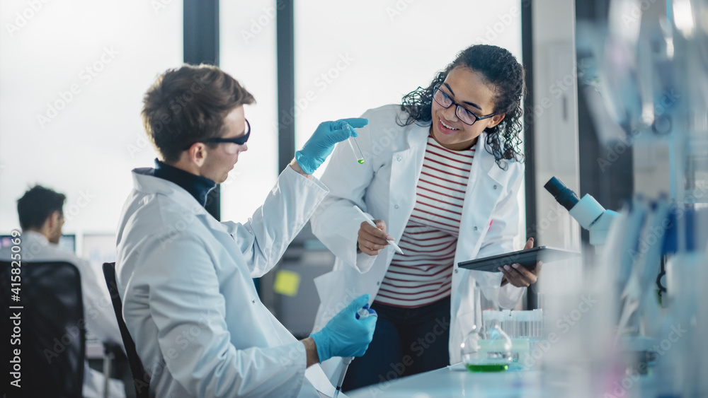 Modern Medical Research Laboratory: Portrait of Two Young Scientists Mixing Liquid Chemicals, Checking Result. Digital Tablet, Talking. Diverse Team of Multi-Ethnic Specialists work in Advanced Lab Modern Medical Research Laboratory: Portrait of Two Young Scientists Mixing Liquid Chemicals, Checking Result. Digital Tablet, Talking. Diverse Team of Multi-Ethnic Specialists work in Advanced Lab