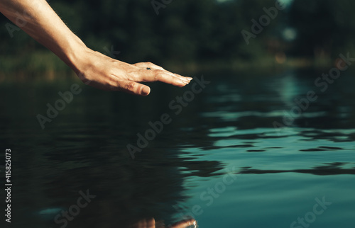 Beautiful woman s palm strokes the water of the lake