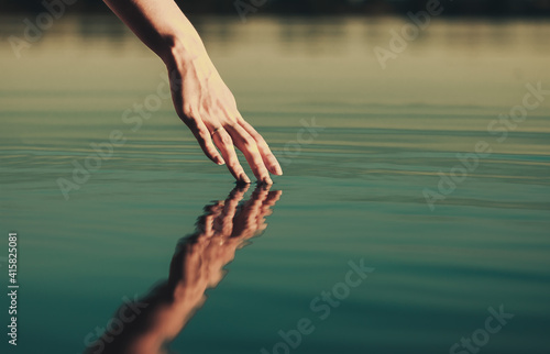 Beautiful woman's palm strokes the water of the lake