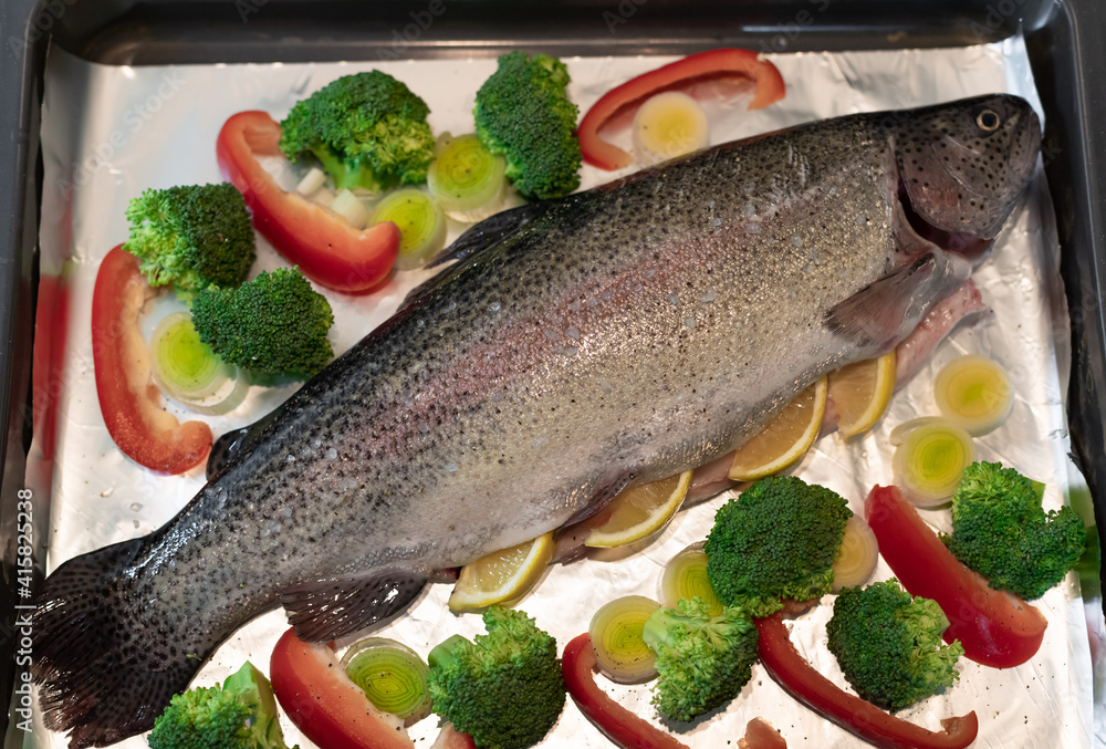 whole raw rainbow trout with broccoli, leek, red pepper and spices on baking tray. Ready for baking. close-up whole raw rainbow trout with broccoli, leek, red pepper and spices on baking tray. Ready for baking. close-up