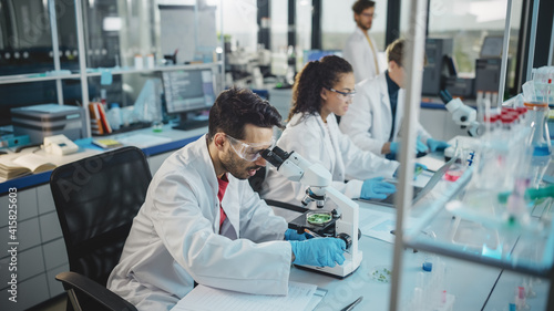 Medical Science Laboratory: Row of Diverse Team of Multi-Ethnic Young Scientists Looking Under Microscope, Analyze Chemicals, Talk, Solving Problems. Biotechnology Specialists working in Advanced Lab